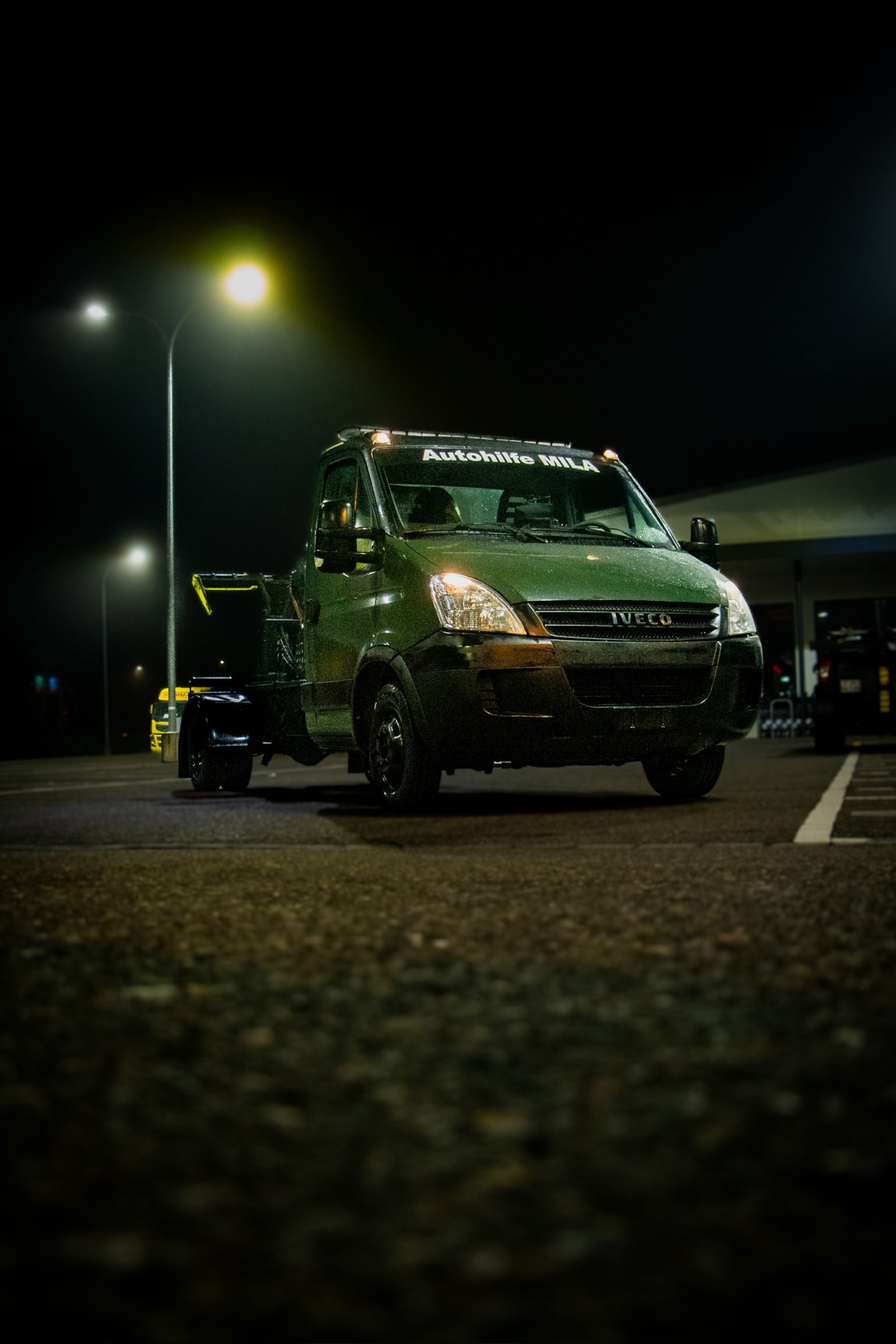 Iveco-Abschleppfahrzeug mit Hubbrille von Autohilfe MILA in Frontansicht bei Nacht