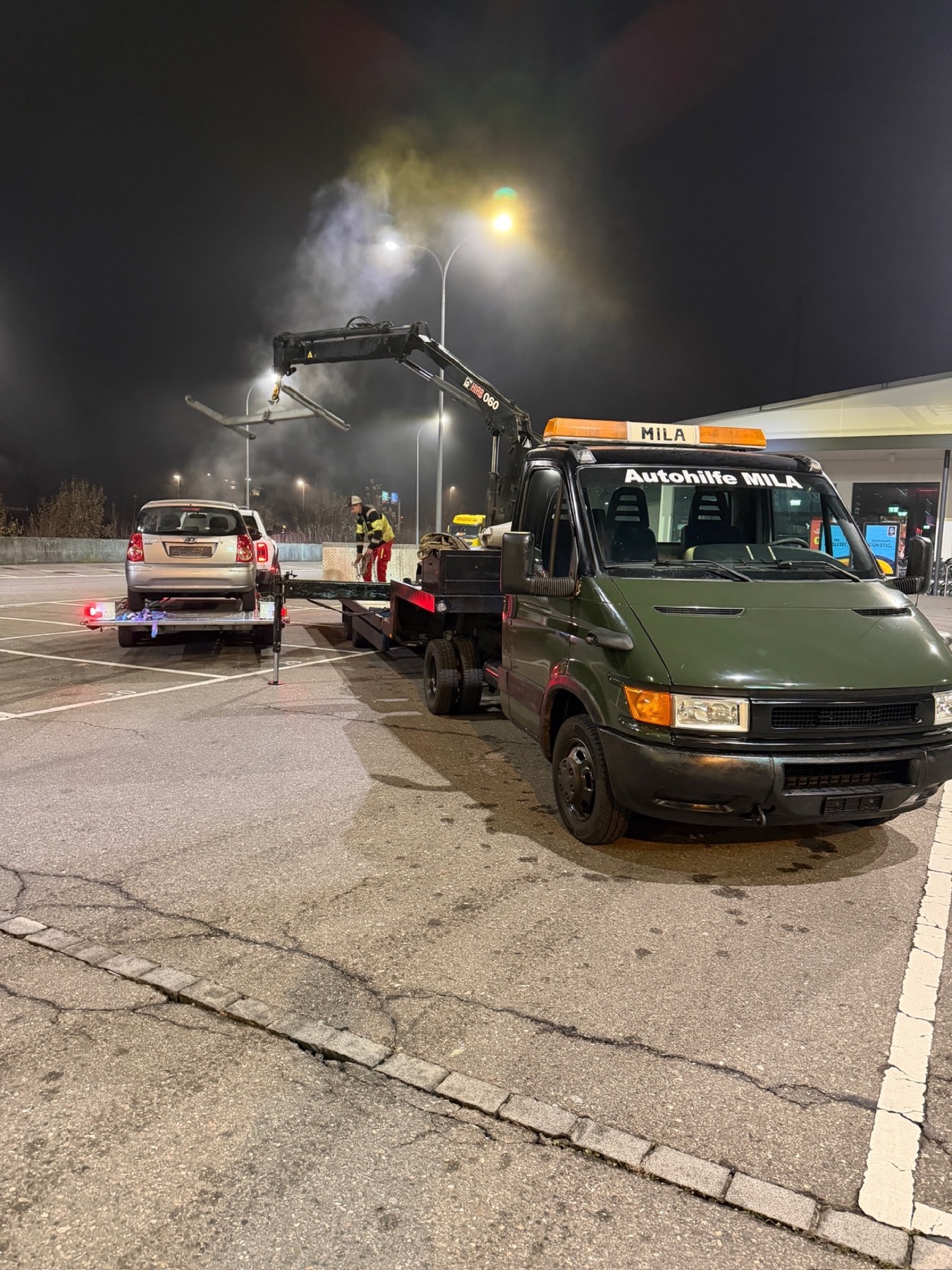 MILA Kranfahrzeug mit Plattform und Fahrzeug bei Nacht