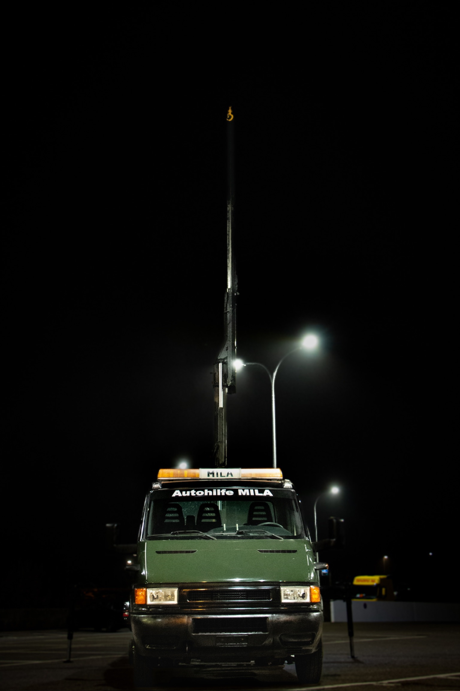 Iveco Daily Plateau-Kran von Autohilfe MILA mit vollständig ausgefahrenem Kran in Frontansicht bei Nacht